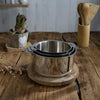 Set de 3 casseroles en inox brillant Du Bruit dans la Cuisine Mutine Cristel empilables sur une table en bois
